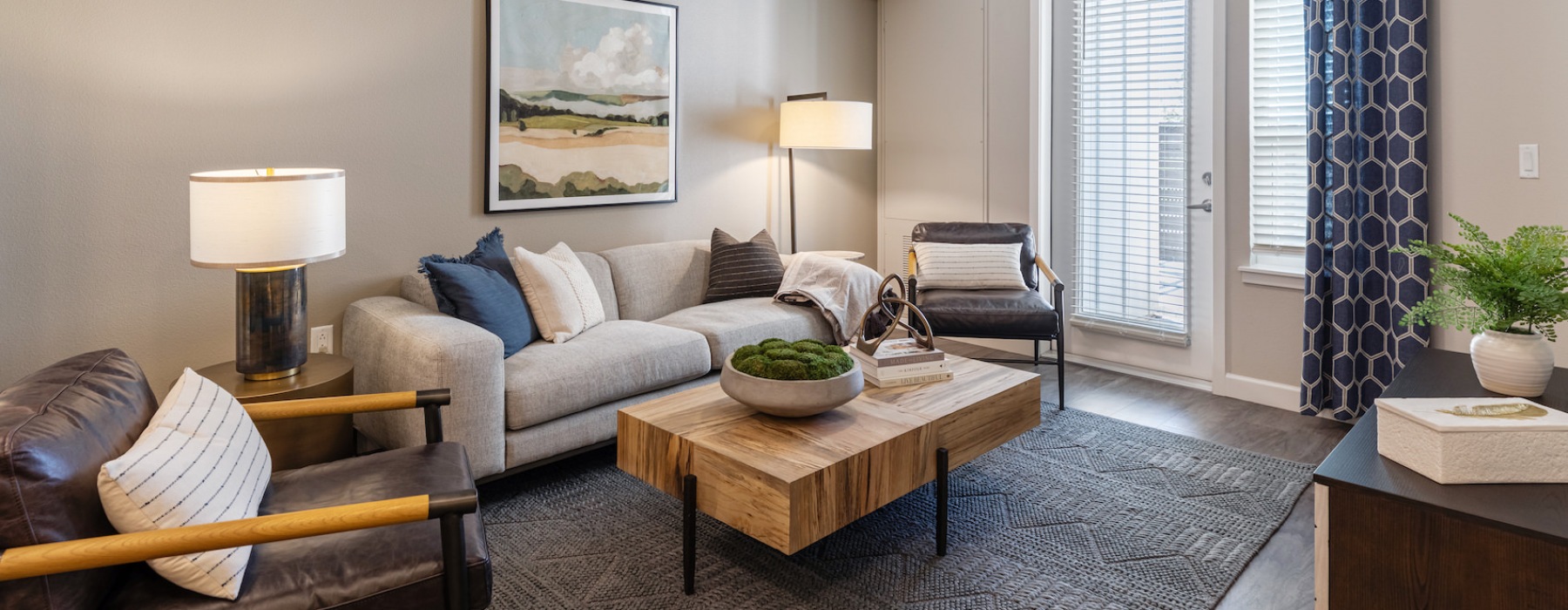 Model living room at our 55 and over apartments in Loveland, CO, featuring a couch, table, and windows with curtains.