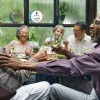 Residents laughing and drinking wine at Avenida at Centerra 55+ apartments in Loveland, featuring overlayed award emblems.